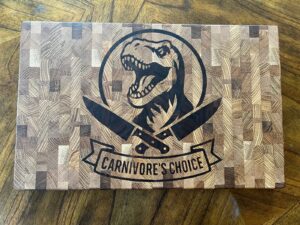 Dinosaur end grain cutting board with Carnivore’s Choice engraving shown in straight overhead view.